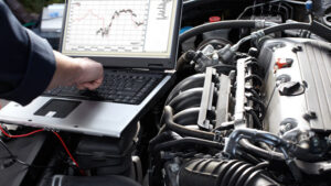 A person working on a laptop in front of an engine.